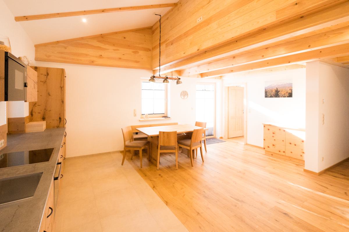 Helle Küche und Essbereich der Ferienwohnung Sauwand mit Holztisch, Sitzbank und Zugang zum Balkon.